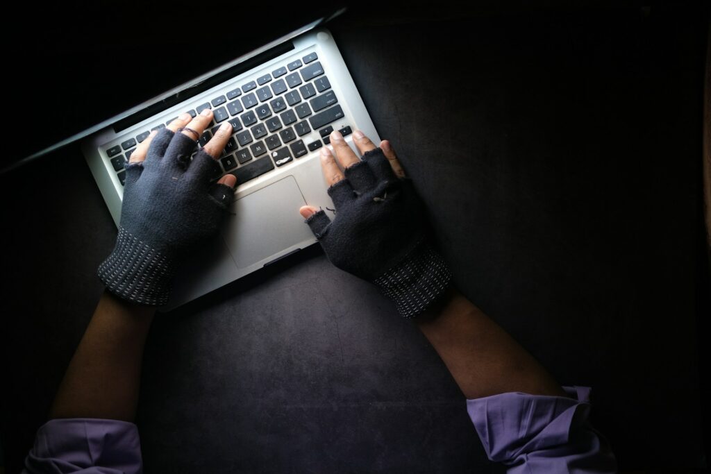 A shadowy figure with gloves using a laptop